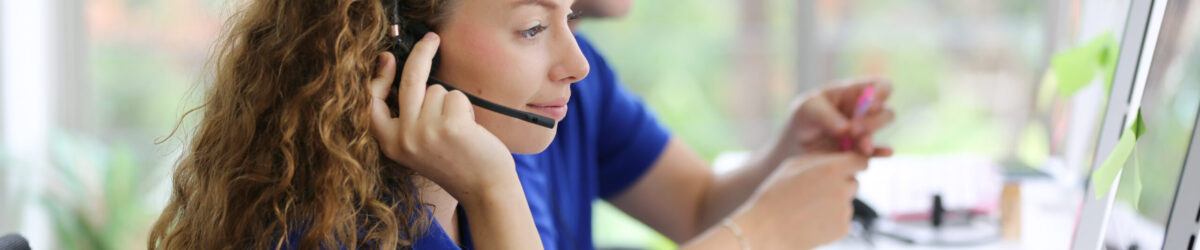 Hotline Support Service. call center operator in headset working with laptop in modern office, looking at computer screen, free space