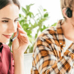 panoramic shot of broker touching headset near man drinking coffee in office